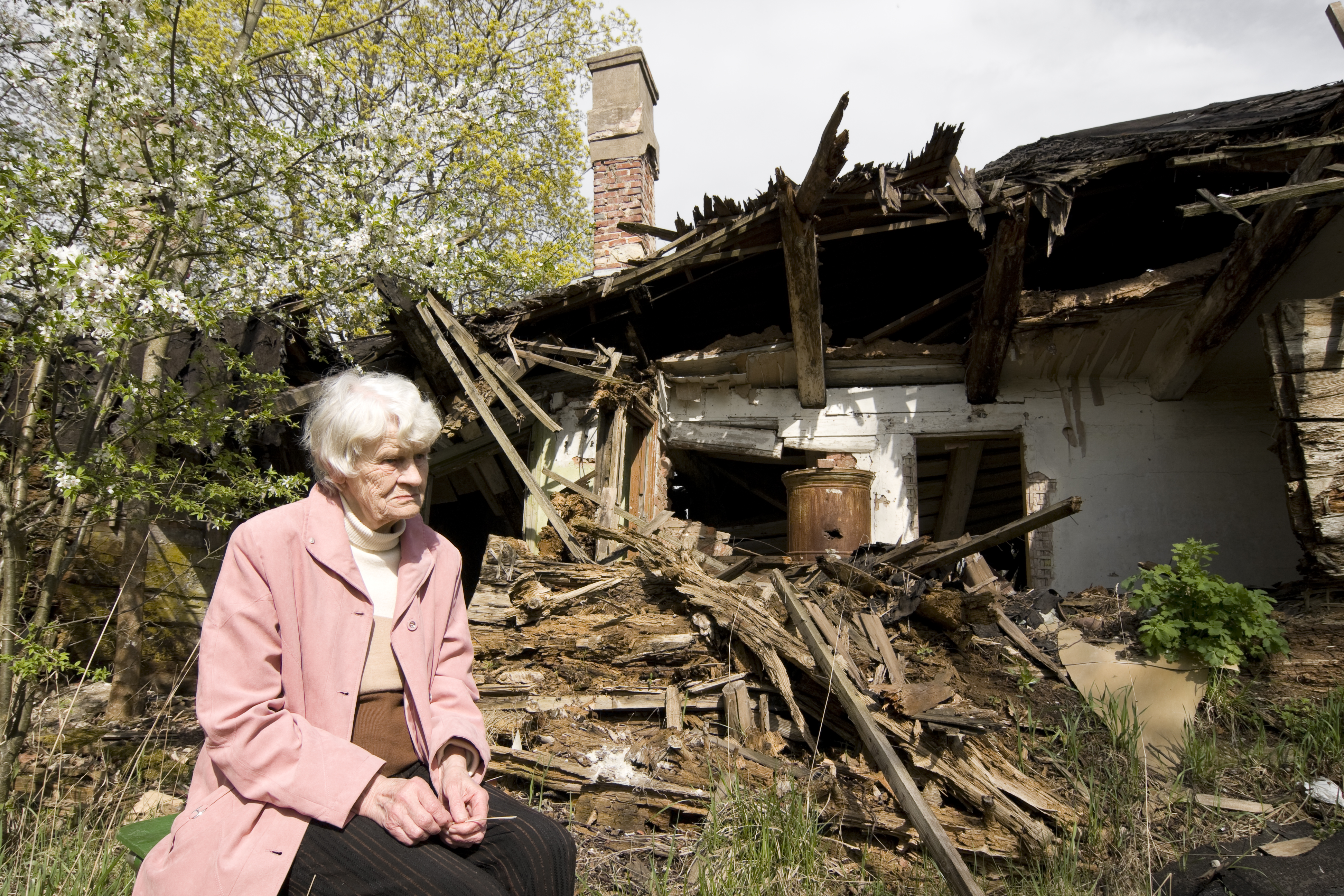 woman in front of her damaged home after a disaster.