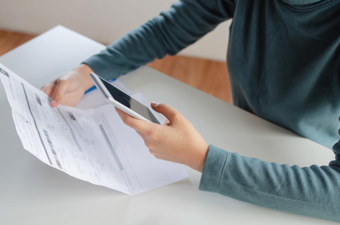 hands of young woman using mobile smart phone for scan and payment online with family budget cost bills on desk in home office, plan money cost saving, investment, business finance, expenses concept